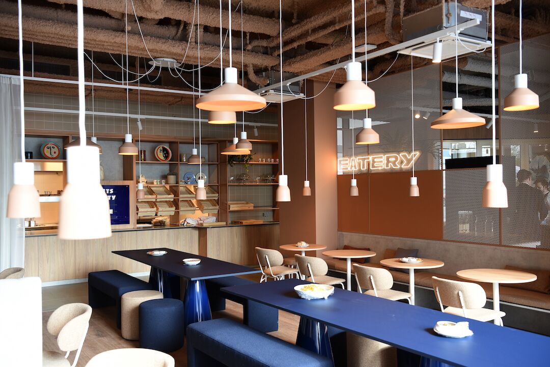 Un interior de restaurante moderno con varias mesas y cabinas para comer, iluminación colgante y un tablero de menú visible.
