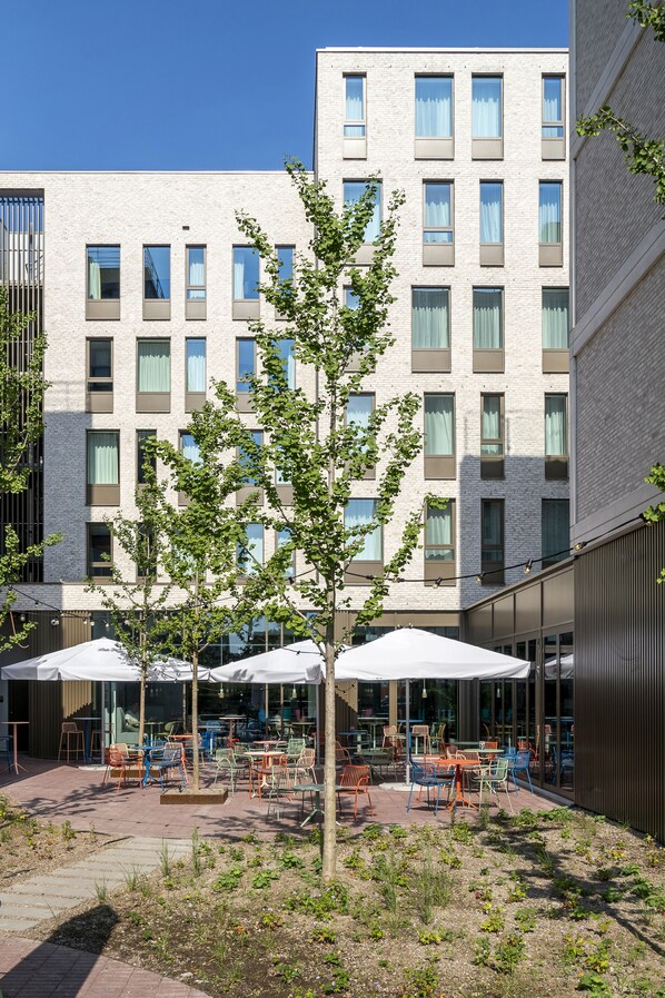 Un pati amb seients exteriors, un arbre i un edifici amb diverses finestres i balcons.