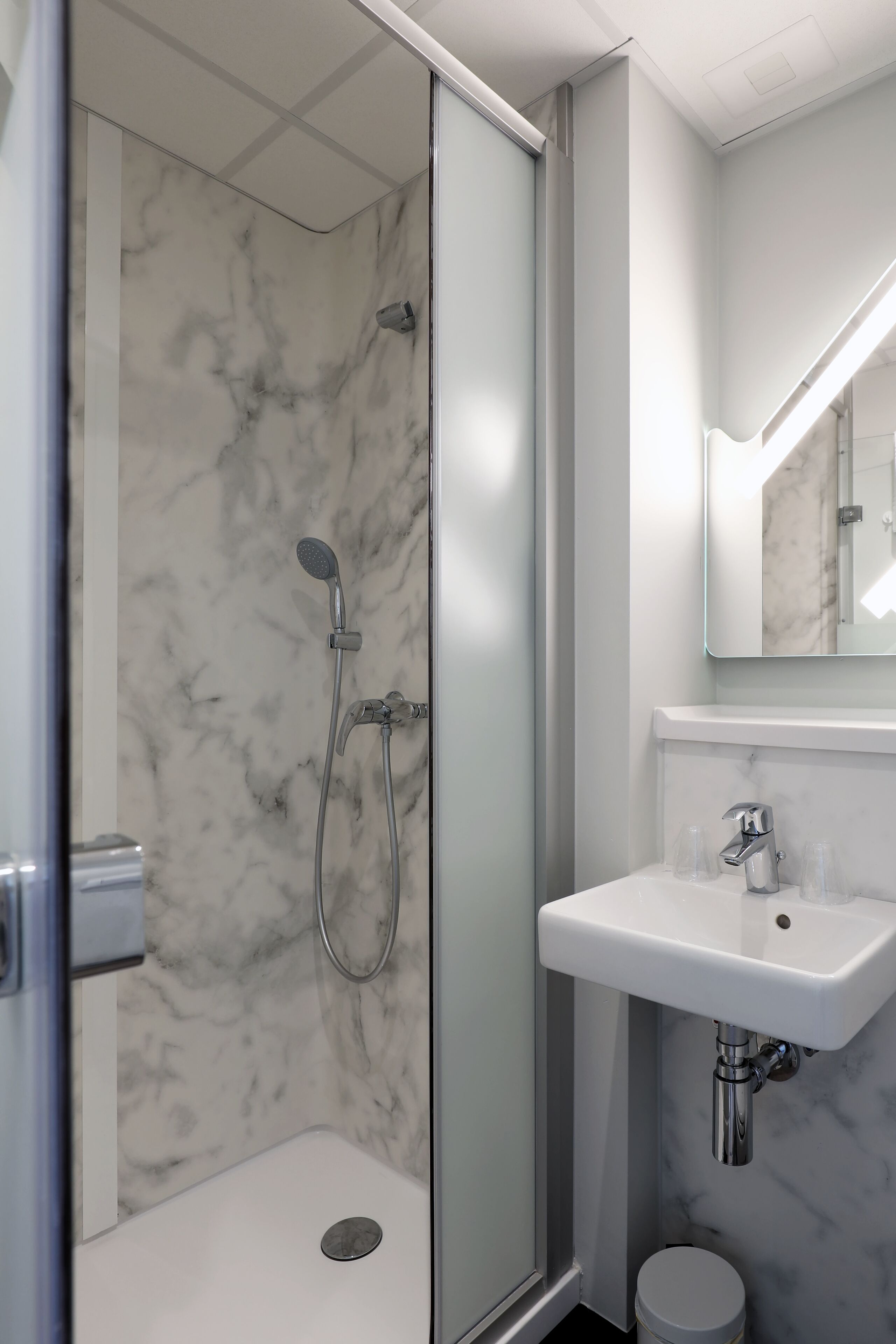 Une salle de bain moderne avec une douche à parois de verre, un lavabo blanc et un pare-baignoire en marbre.