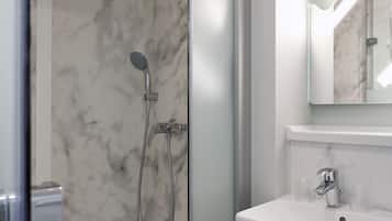 Une salle de bain moderne avec une douche à parois de verre, un lavabo blanc et un pare-baignoire en marbre.