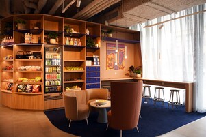 Een gezellig zithoekje met een ronde tafel, twee stoelen en een bank met krukjes. Planken langs de muren zijn gevuld met snacks en drankjes.