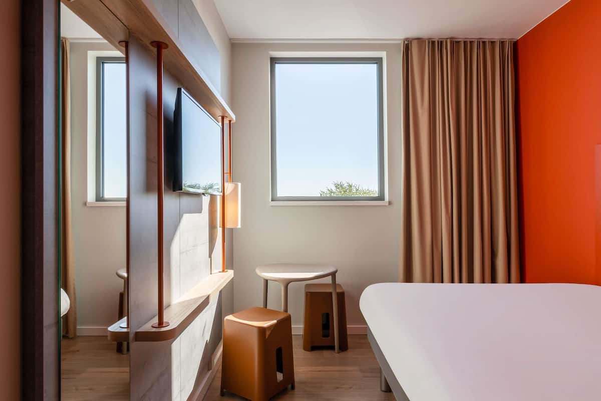 Habitació d'hotel moderna amb un llit gran, una televisió penjada en un panell de fusta, una taula petita i un tamboret.