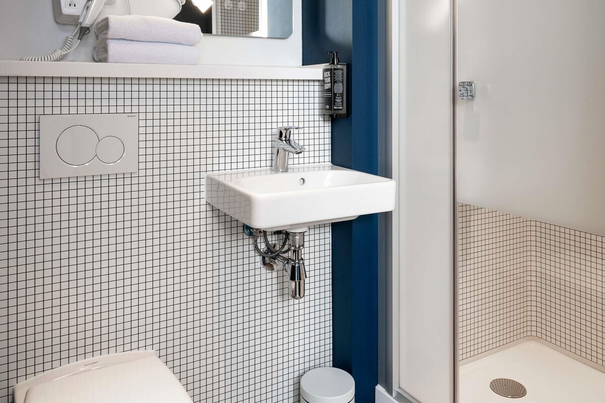 Un baño con lavamanos blanco, espejo, secador de pelo y perchero para toallas.