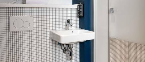 Un baño con lavamanos blanco, espejo, secador de pelo y perchero para toallas.
