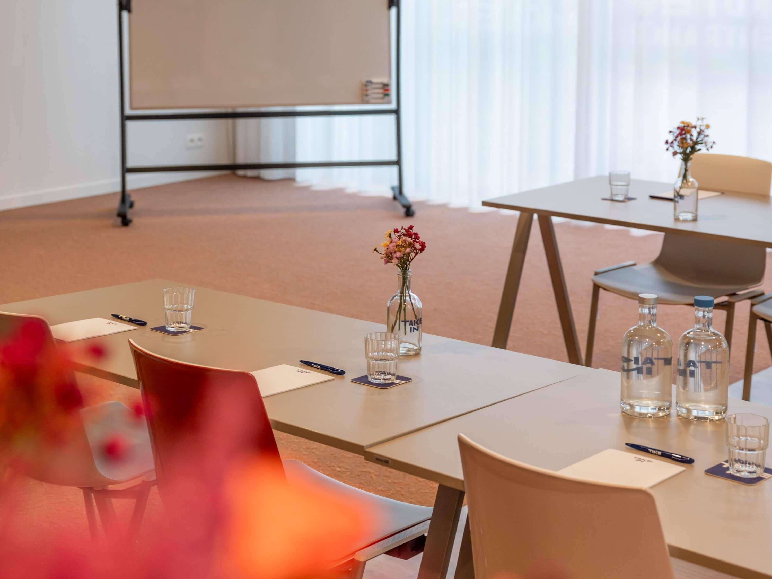 Una sala de conferències amb taules, cadires, una pissarra i un ram de flors.