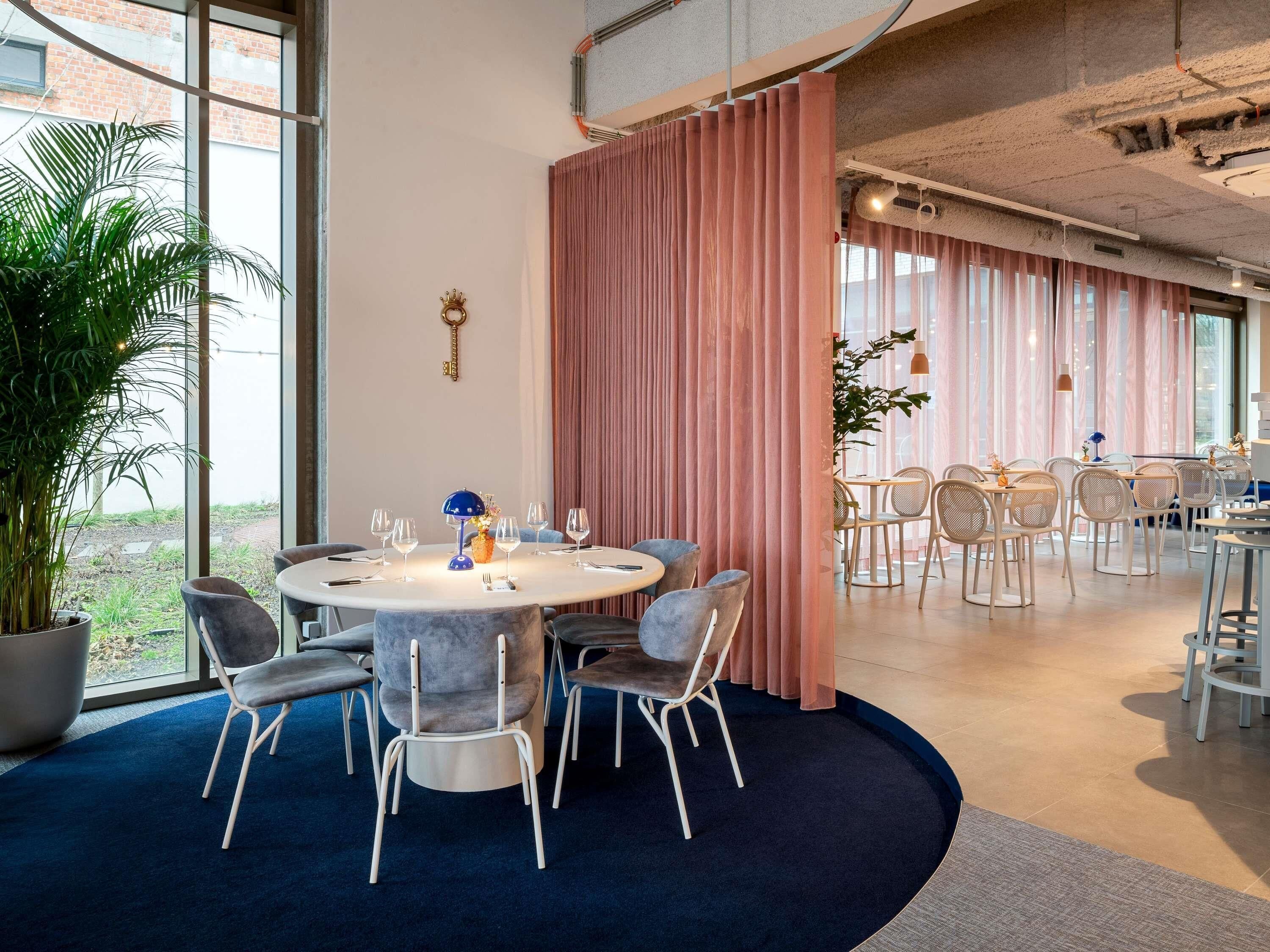 A modern dining area with round tables, chairs, and a large potted plant.
