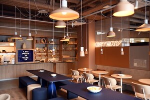 A modern cafe with multiple seating areas, including tables and benches, and a visible counter with a neon sign.