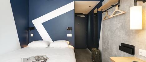 A modern hotel room with a bed, a desk, and a hanging light fixture.