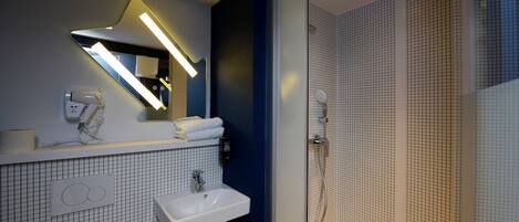Un baño moderno con lavamanos blanco, espejo con iluminación integrada, cabina de ducha y toallero.