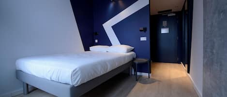 A modern bedroom with a bed, a small stool, and a door leading to another room.