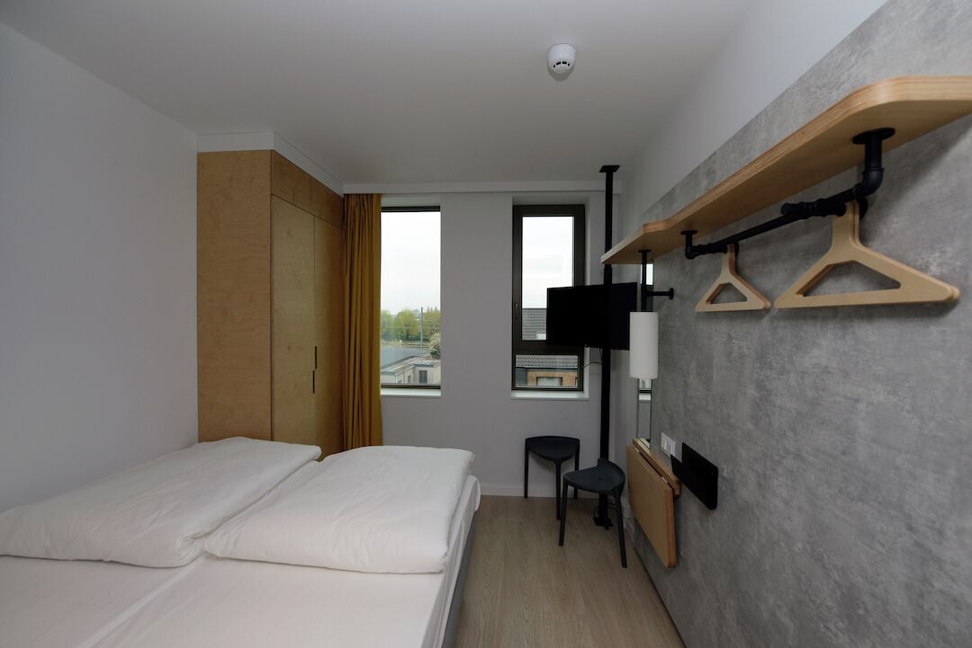 A modern hotel room with a bed, wardrobe, TV, and a wall-mounted drying rack.