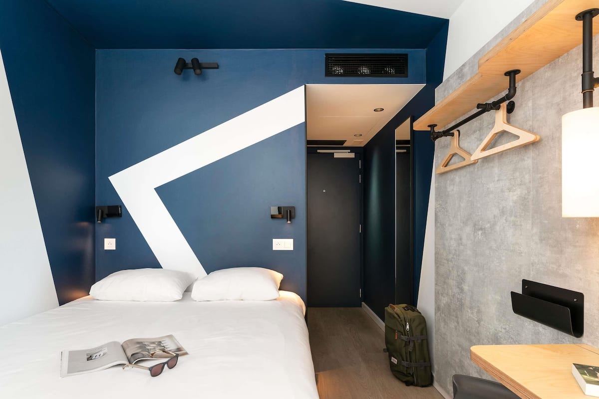 Una habitación de hotel moderna con cama, escritorio, silla, lámpara colgante y perchero.