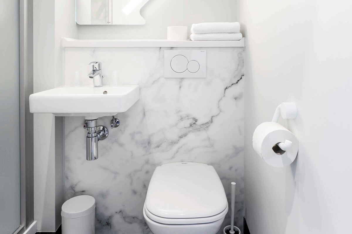 Un baño pequeño con lavamanos, inodoro y paredes de mármol blancos.
