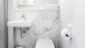 Un baño pequeño con lavamanos, inodoro y paredes de mármol blancos.