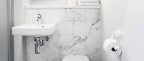 A compact bathroom with a white sink, toilet, and marble walls.