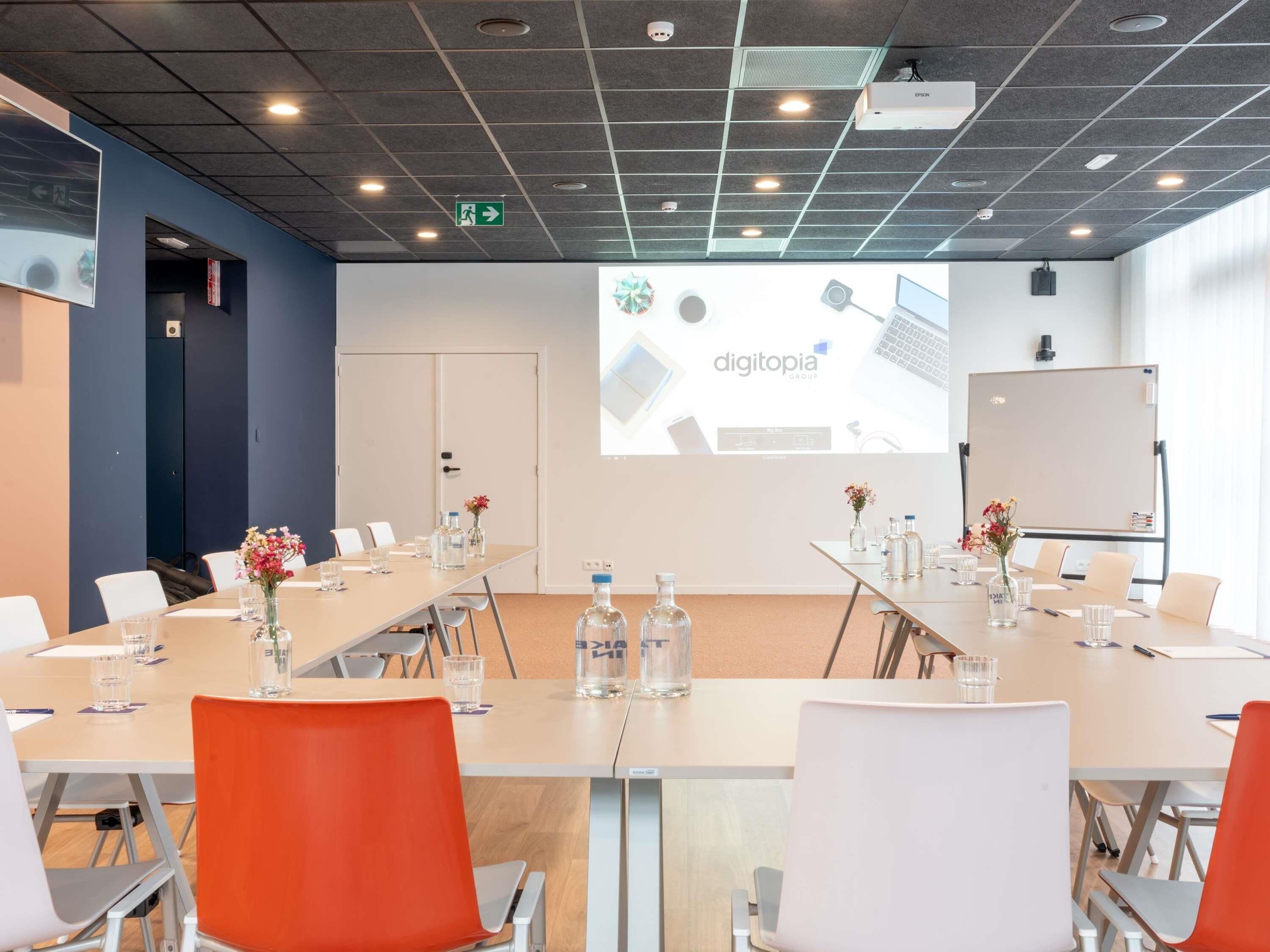 Een vergaderruimte met een lange tafel, stoelen, een whiteboard en een projectiescherm waarop 'digitopia' staat.