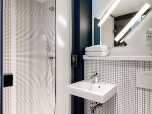 Un baño moderno con pared de ducha de diseño tipo cuadrícula, un lavamanos blanco y un espejo con iluminación integrada.