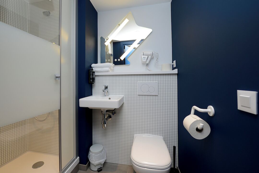 Une salle de bain moderne équipée d’une douche, d’un lavabo, de toilettes et d’un miroir avec éclairage intégré.