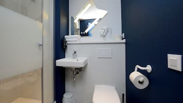 Une salle de bain moderne équipée d’une douche, d’un lavabo, de toilettes et d’un miroir avec éclairage intégré.