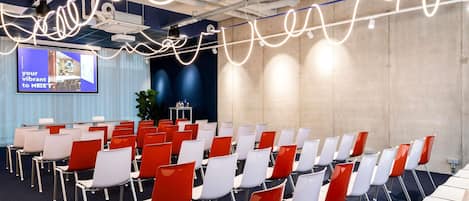 A conference room with rows of chairs, a projector screen, and a large plant.