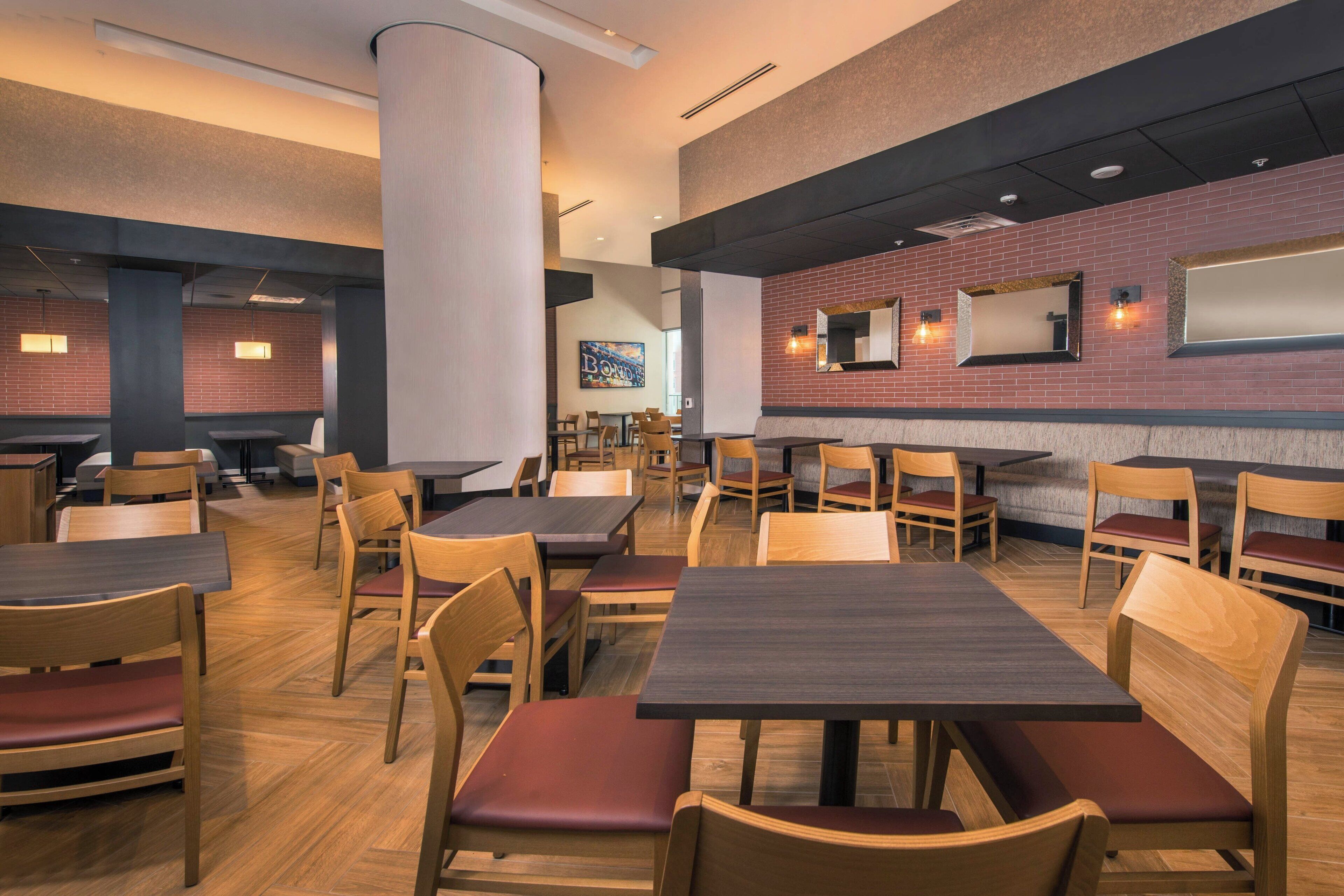 Un restaurante con mesas y sillas de madera, paredes de ladrillo y luminarias modernas.