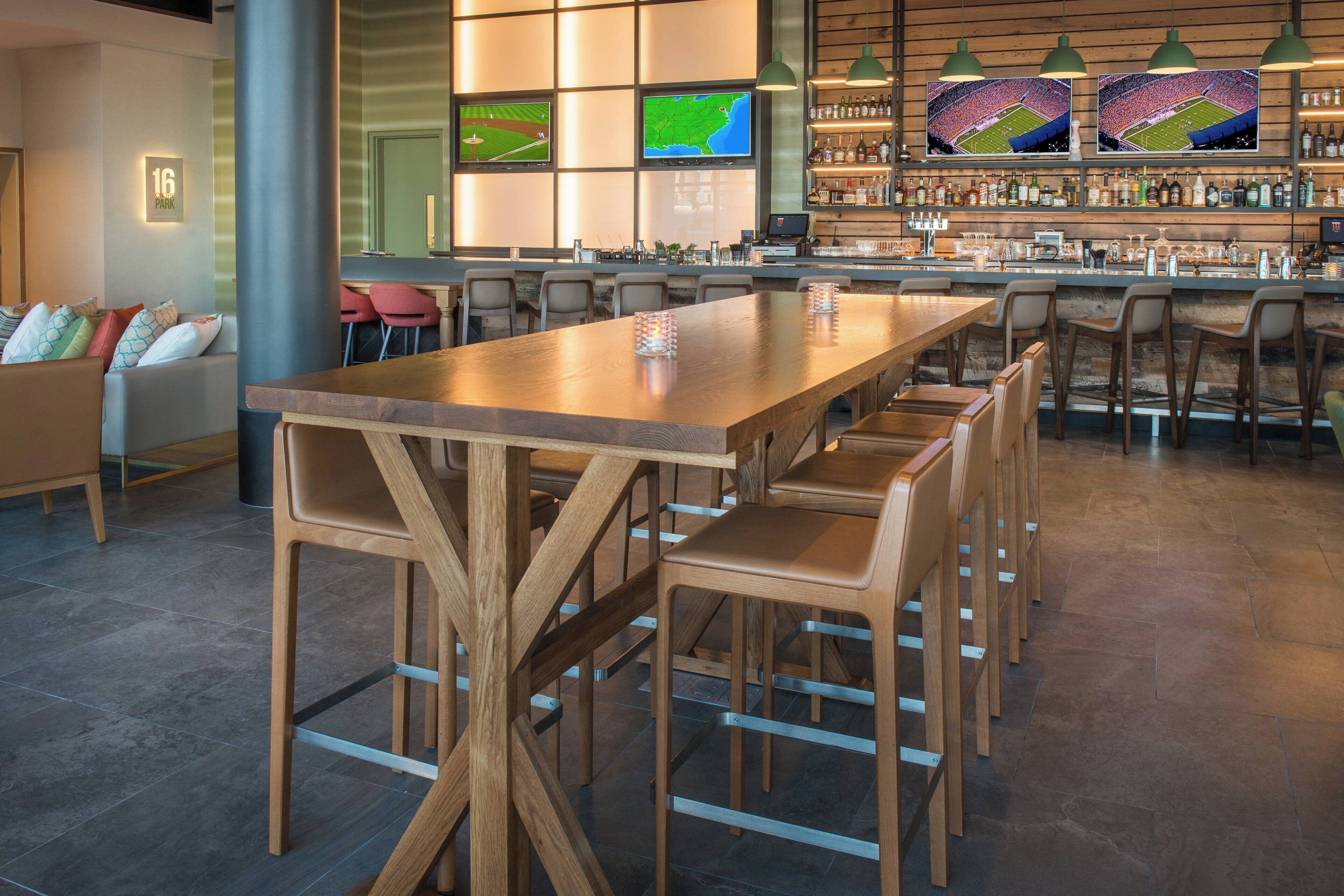 A modern bar area with a long wooden table, multiple bar stools, and a bar counter.