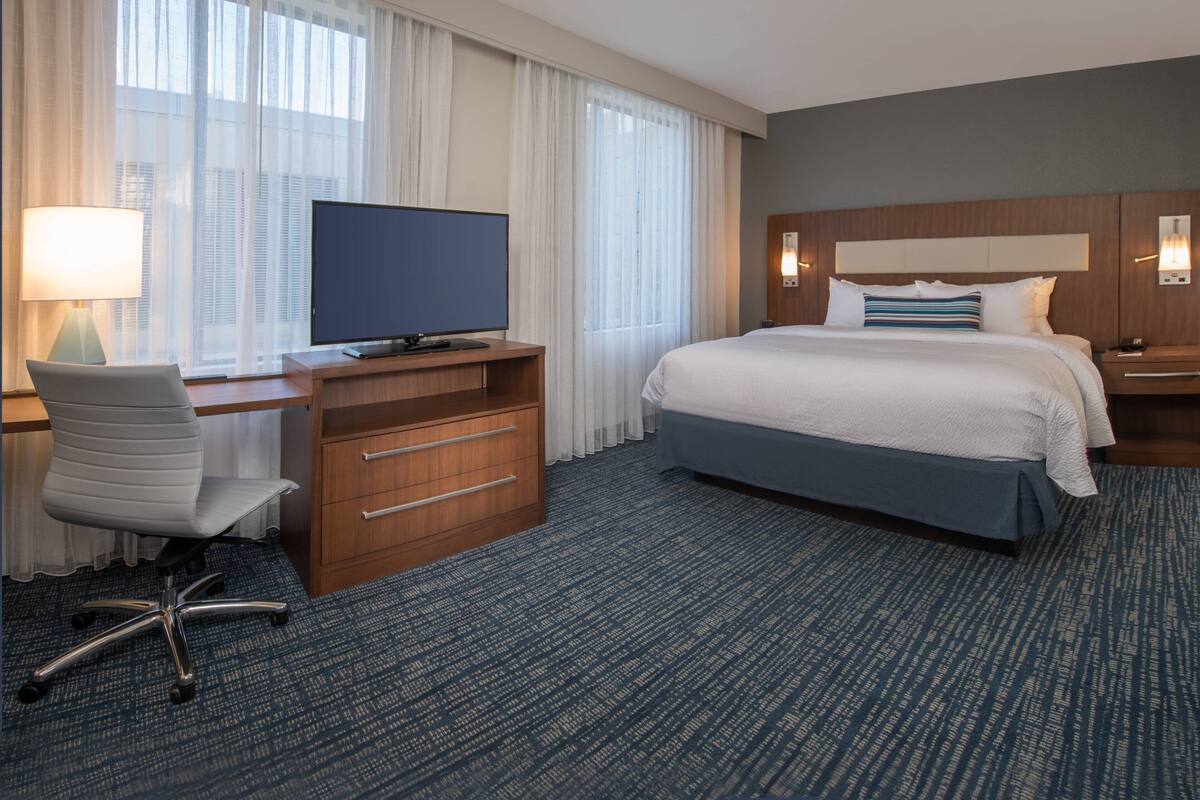 Habitación de hotel con una cama grande, un escritorio con televisor, una silla y un aparador.