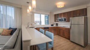 Una cocina moderna con una isla central, armarios de madera, electrodomésticos de acero inoxidable y vistas a la ciudad a través de amplias ventanas.