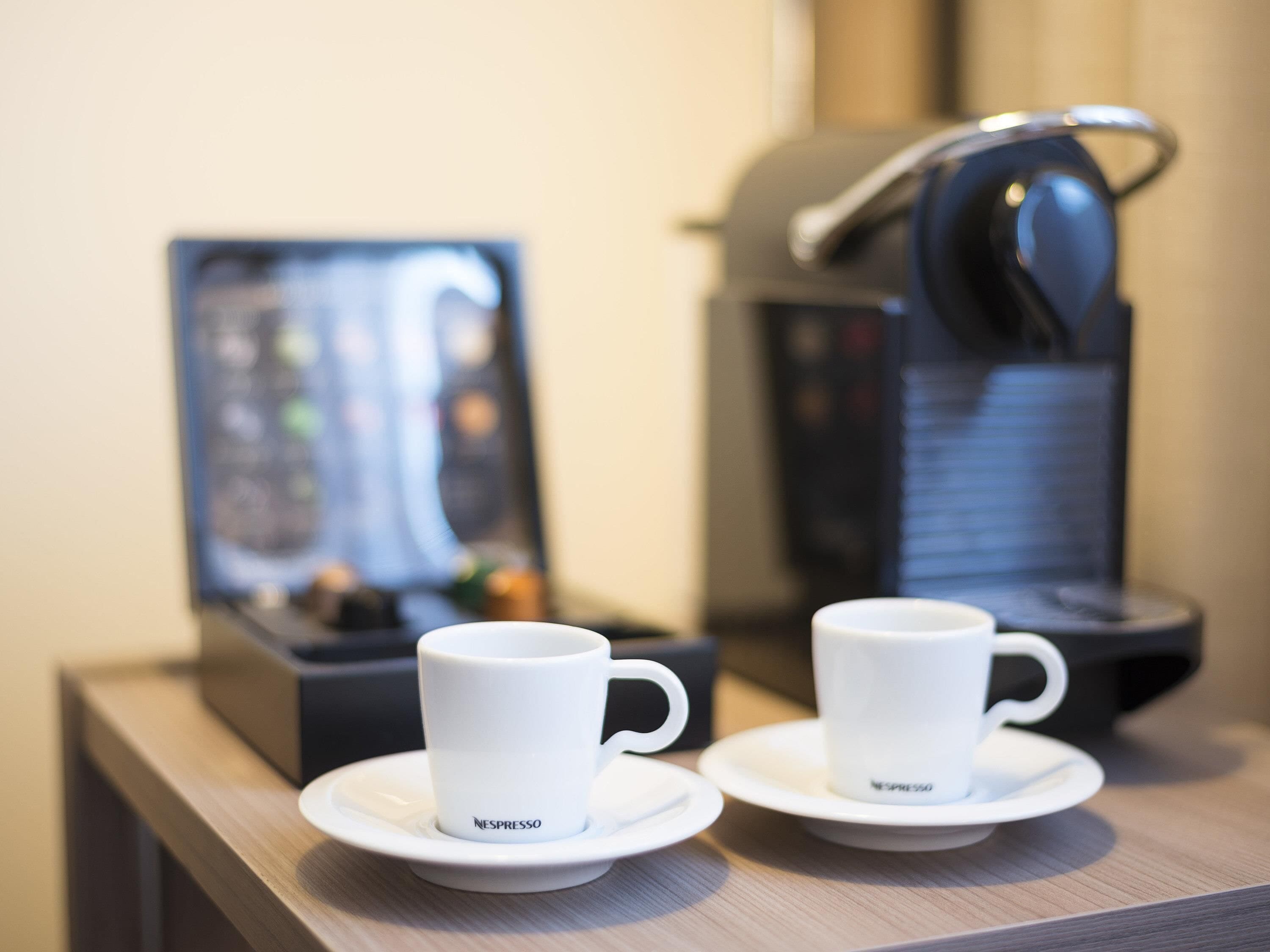 Two white Nespresso cups on saucers on a wooden table, with a Nespresso machine in the background.