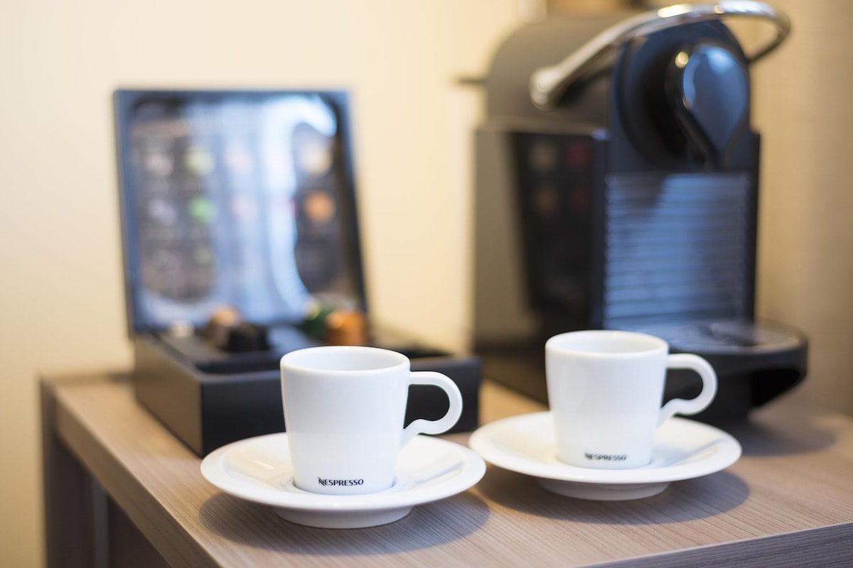 Two white Nespresso cups on saucers on a wooden table, with a Nespresso machine in the background.