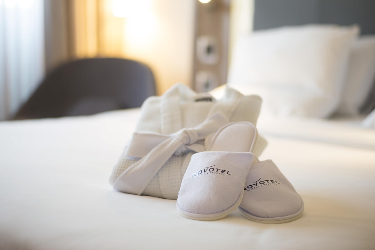A neatly made bed with a pair of slippers and a robe on it.