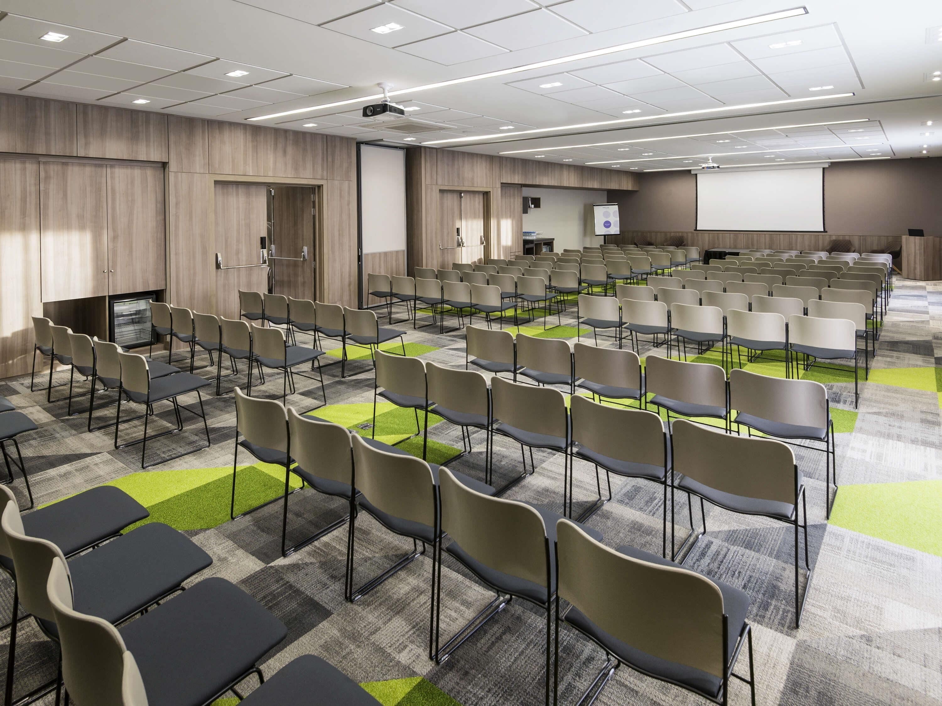 A conference room with rows of chairs, a projector, and a screen.