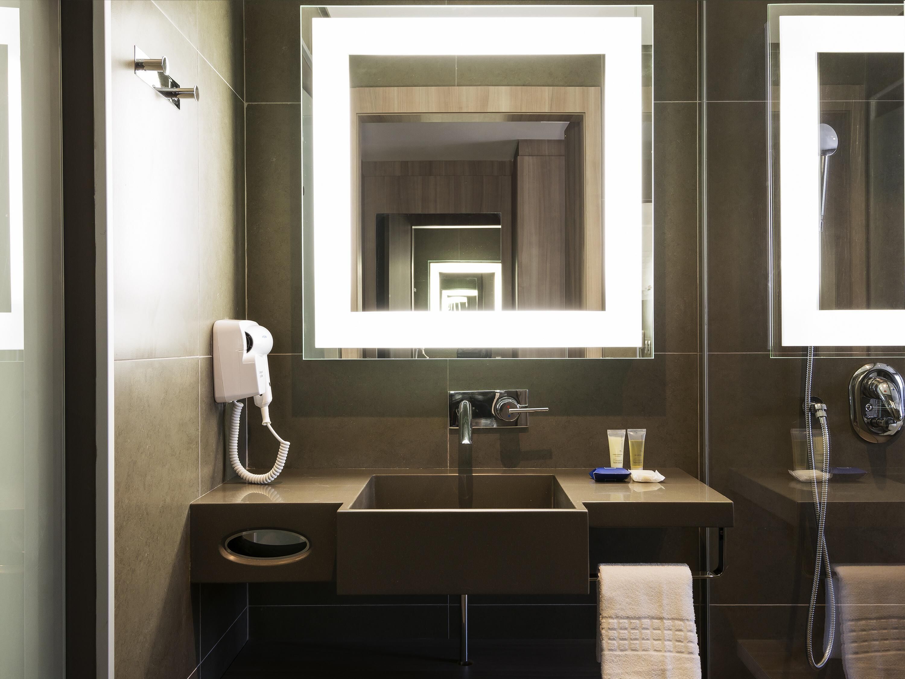 A modern bathroom with a large mirror, a sink, a hairdryer, and a shower.