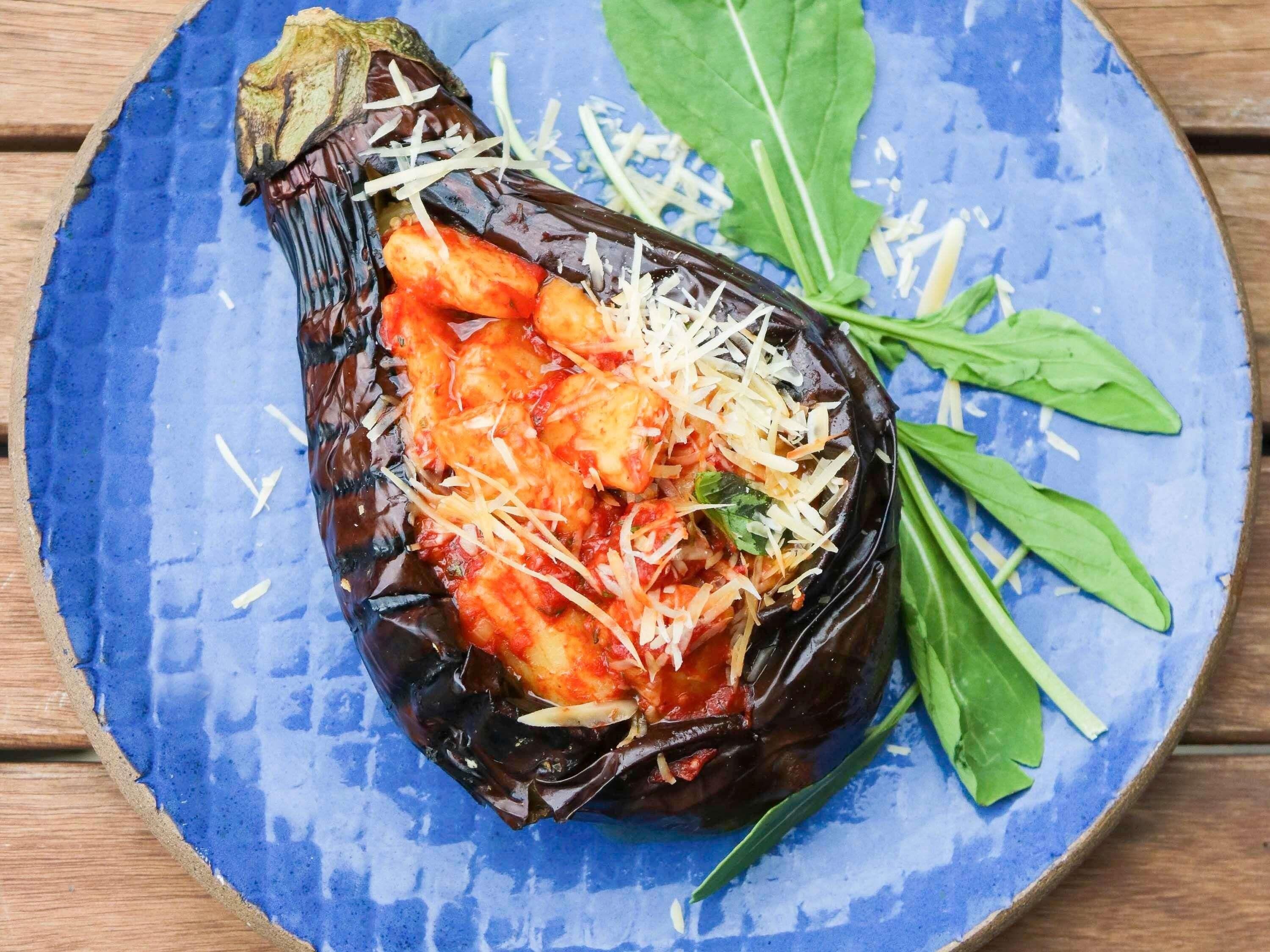 A stuffed eggplant on a blue plate with green leaves.