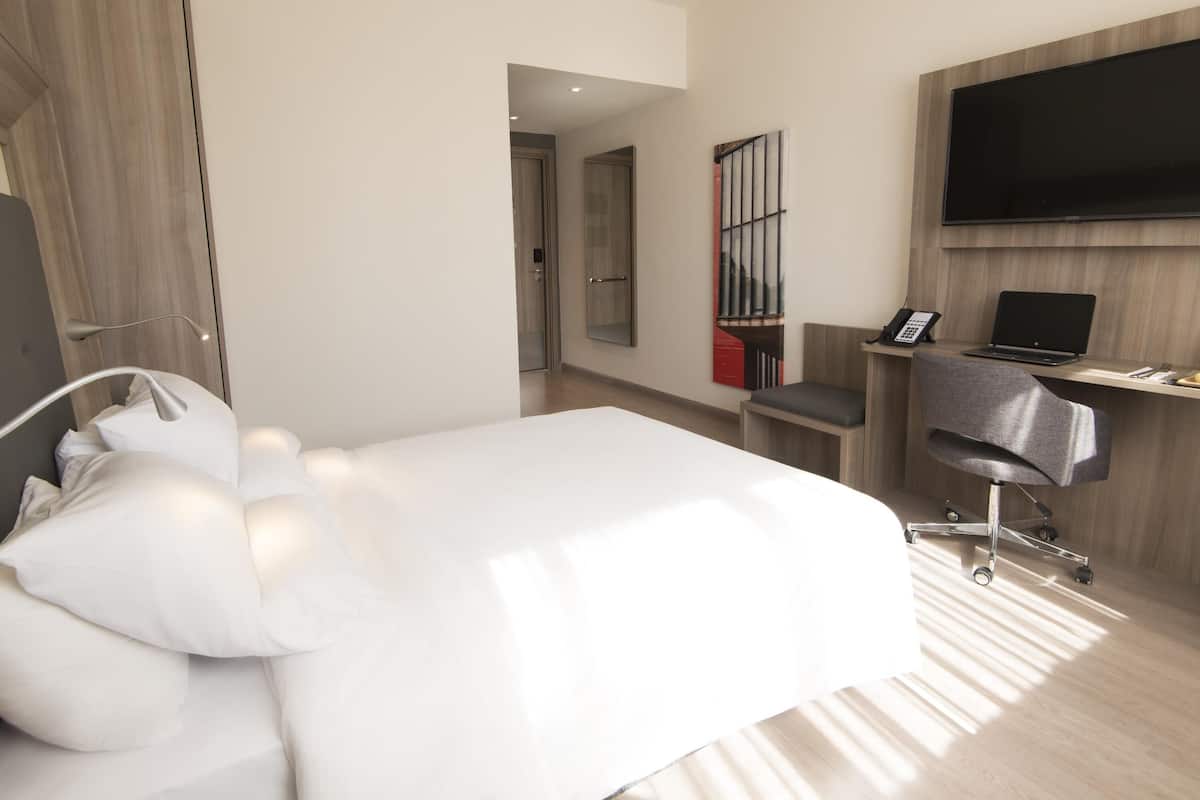 Une chambre d’hôtel moderne équipée d’un grand lit, d’un bureau avec un ordinateur portable, d’une chaise, d’une télévision et d’un miroir.