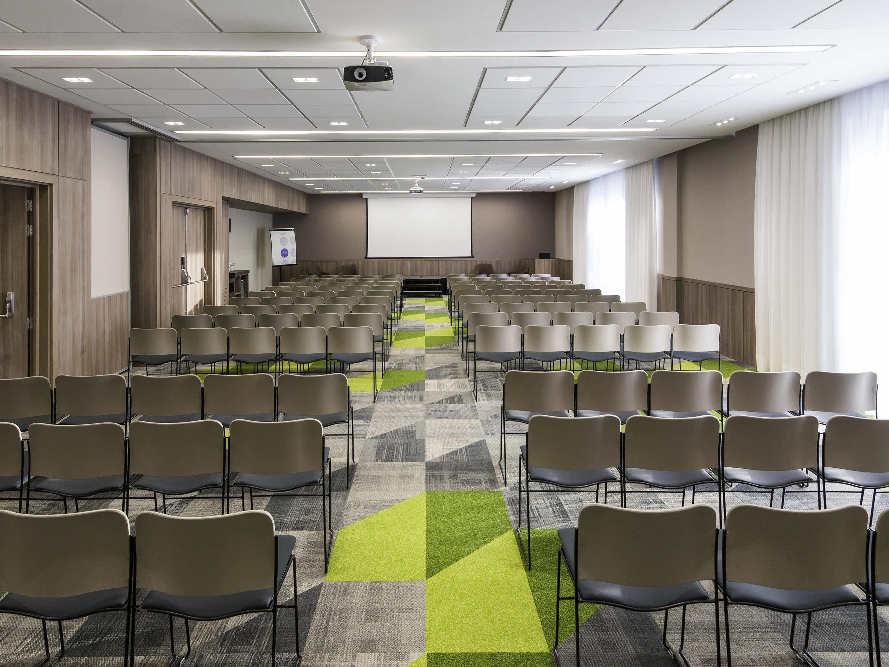 Une salle de conférence avec des rangées de chaises, un projecteur et un écran.
