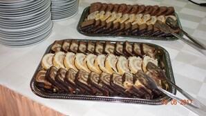 Una mesa de buffet con dos fuentes de pasteles en rebanadas, una pila de platos y un mantel a cuadros.