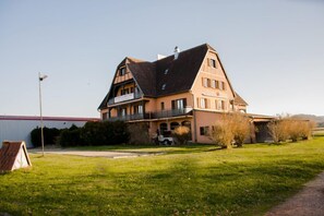 A large, two-story building with a prominent balcony on the second floor, a garage, and a well-maintained lawn. - Hôtel L'Écu D'Alsace (Gresswiller)