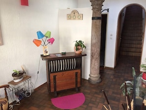 Quarto com um banco de madeira, uma pequena mesa com abajur, uma planta em vaso e um relógio de parede.