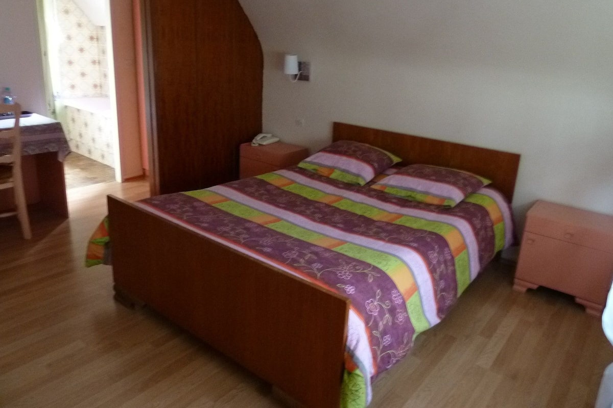 A bedroom with a wooden bed, a nightstand, a desk, and a chair.