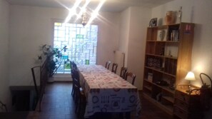 A dining area with a long table, chairs, a bookshelf, and a window with a view. - Hotel aux deux clefs (Marmoutier)
