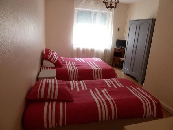 A bedroom with two beds, a wardrobe, a television, and a window with curtains. - Hotel aux deux clefs (Marmoutier)