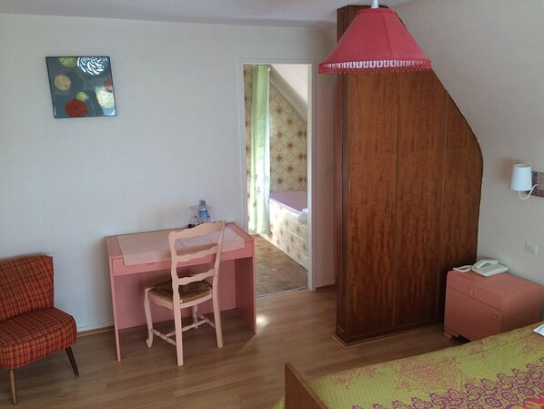 Habitación de hotel con un escritorio de madera, una silla, una cama con colcha verde estampada, una lámpara roja y un teléfono montado en la pared.
