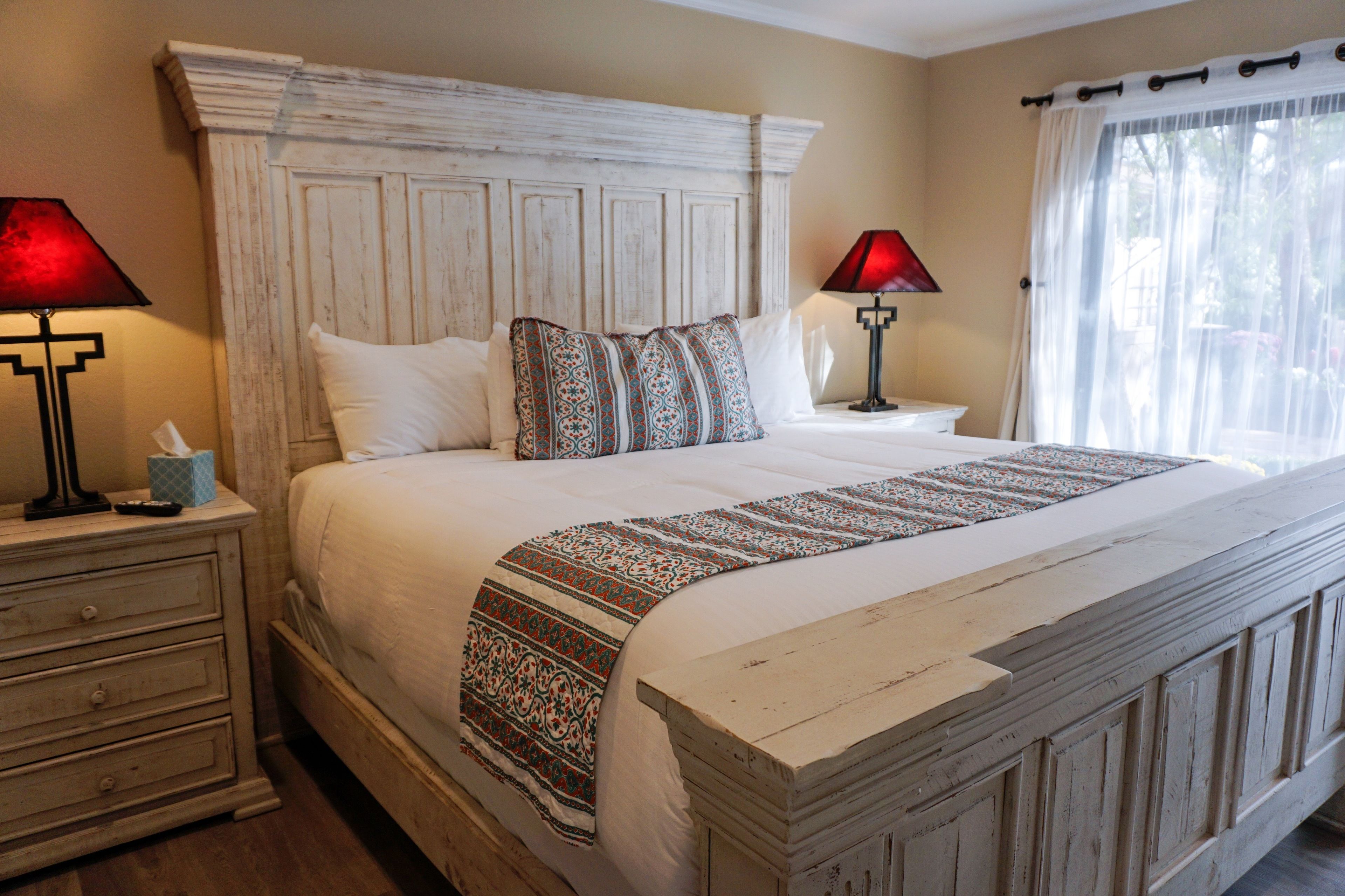 A neatly made bed with a patterned throw, a wooden headboard, and two bedside lamps.