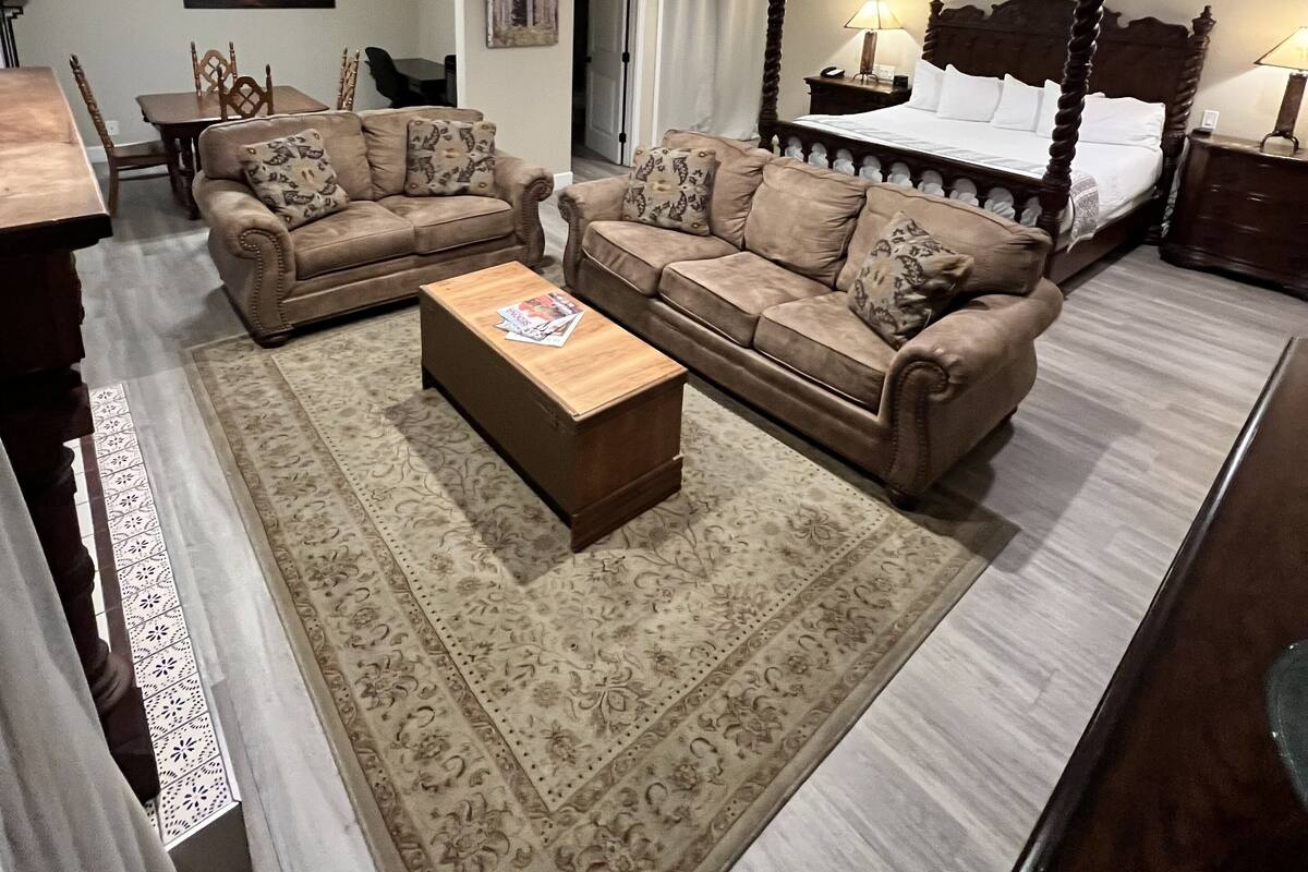A well-lit living room with a large bed, two sofas, a coffee table, and a dining area.