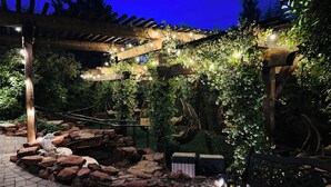 A garden with a pergola, hanging chairs, and a stone wall.
