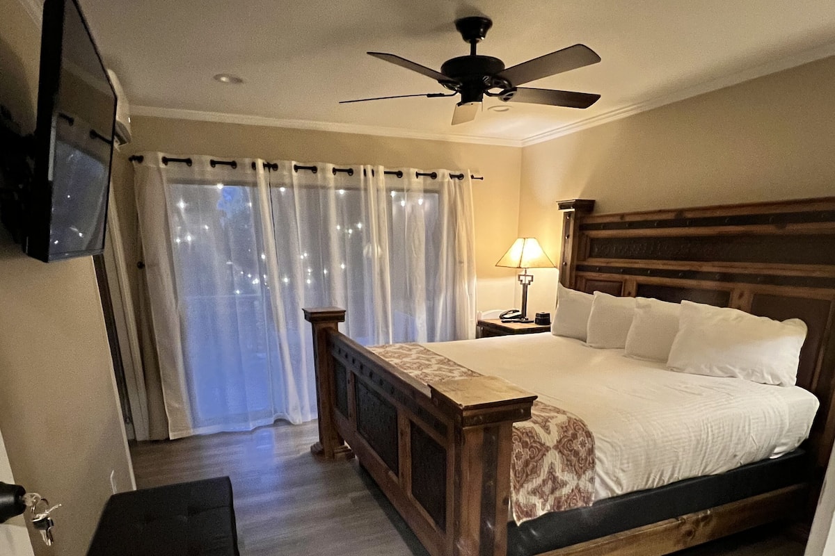 A bedroom with a wooden bed, a ceiling fan, a TV mounted on the wall, and a nightstand with a lamp.