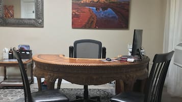 Sala de conferências com uma mesa redonda, quatro cadeiras, um computador e uma pintura de uma paisagem.