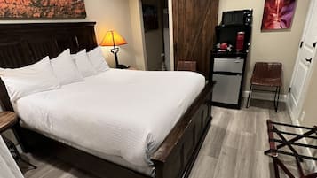 Una camera da letto con un letto grande, un ventilatore a soffitto, un comodino, una lampada, un tavolino, un frigorifero, una sedia e una porta.