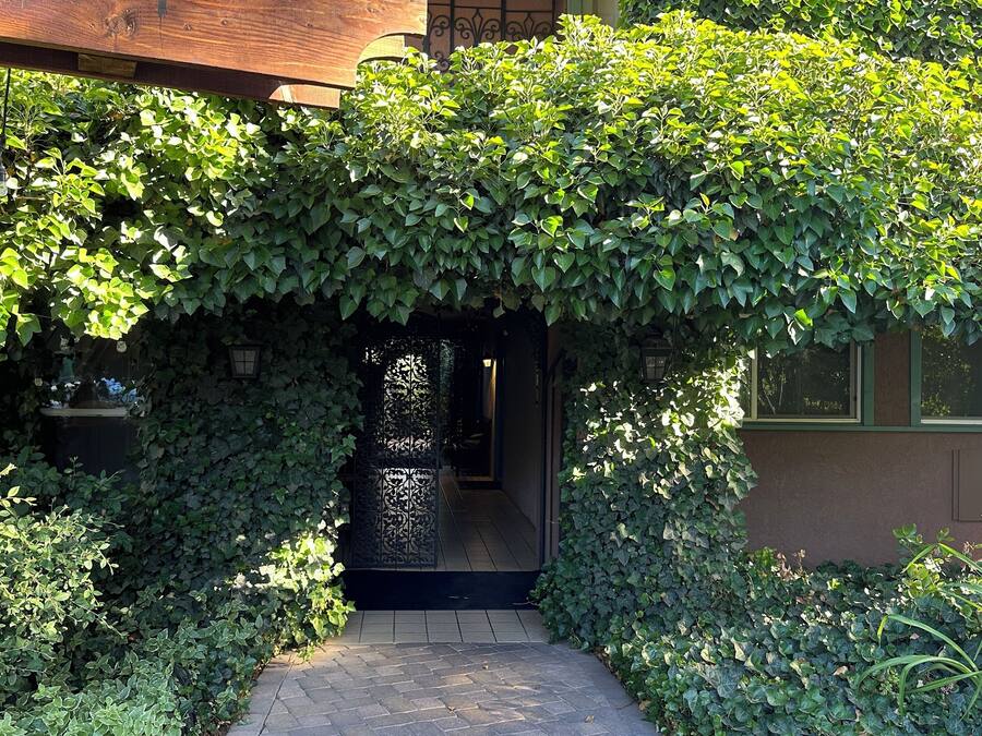 A covered entrance with a wooden structure, a metal gate, and a pathway leading to a door.